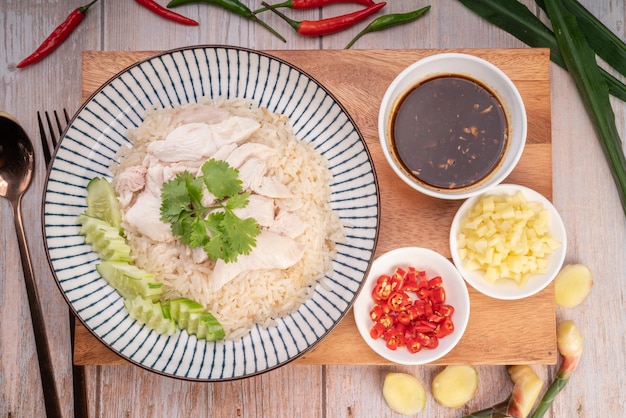 Steamed rice topped with chicken on wooden background Hainanese chicken rice served with chili sauce