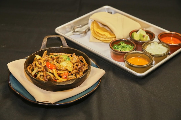 Steaming Beef Fajitas in Skillet with Condiments Side View