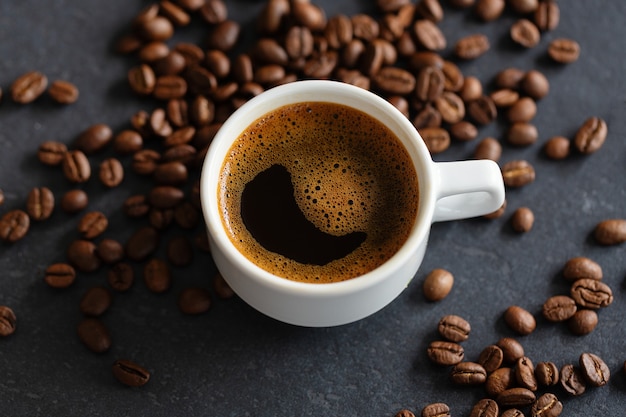 Steaming espresso cup on coffee beans background. Closeup