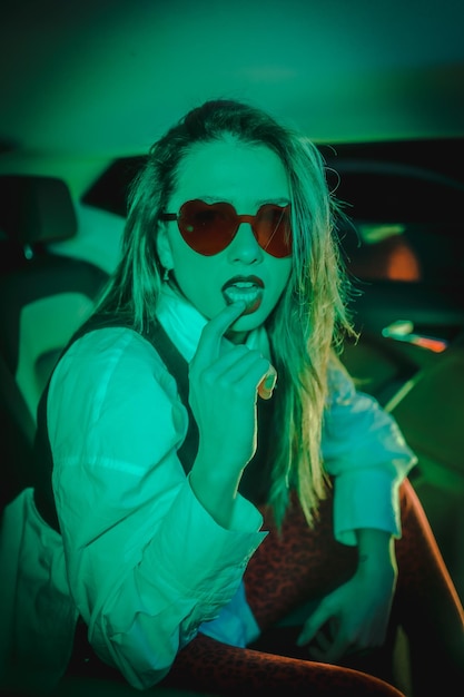 Stedelijk met groene neons achter in een auto van een jonge blonde vrouw met een hartbril