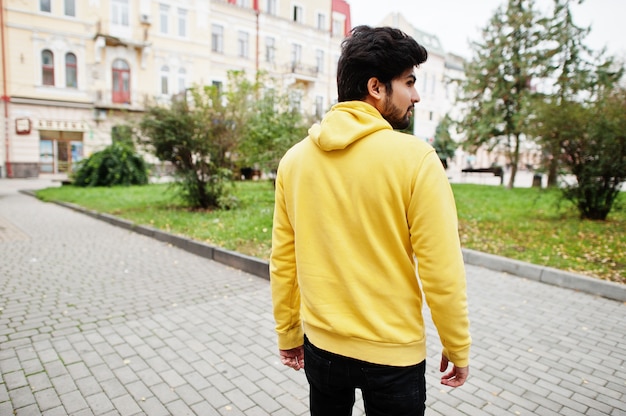 Stedelijke jonge hipster Indiase man in een trendy geel sweatshirt. Koele Zuid-Aziatische jongen dragen hoodie lopen op straat.