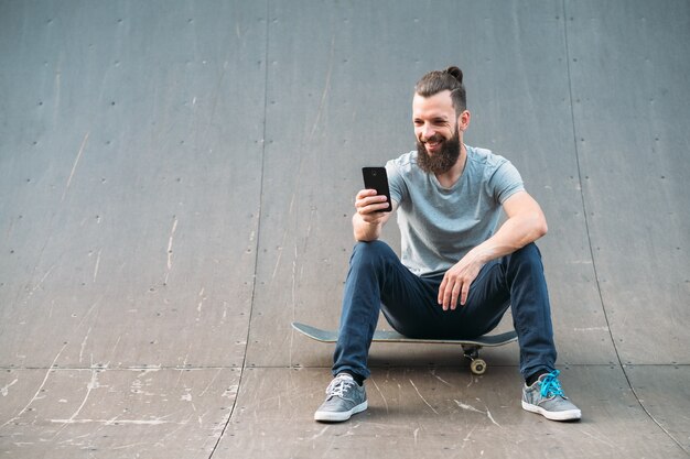 Stedelijke man. Vrije tijd en levensstijl. Glimlachend bebaarde hipster zittend op een skateboard en het nemen van selfie.