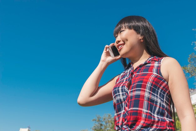 Stedelijke slimme casual jonge Aziatische vrouw praten op smartphone. Gelukkige vrouwelijke volwassene die op mobiele telefoon spreekt.