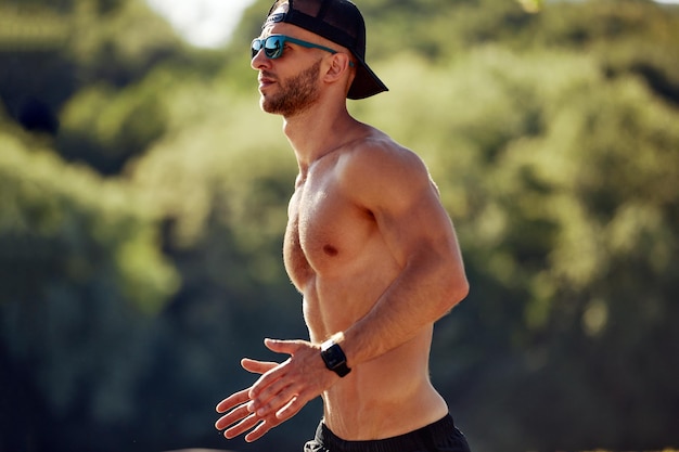 Stedelijke sporten Sportieve man shirtloos joggen voor fitness in het stadspark op een mooie zomerdag