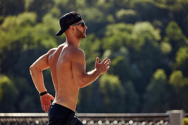 Stedelijke sporten Sportieve man shirtloos joggen voor fitness in het stadspark op een mooie zomerdag