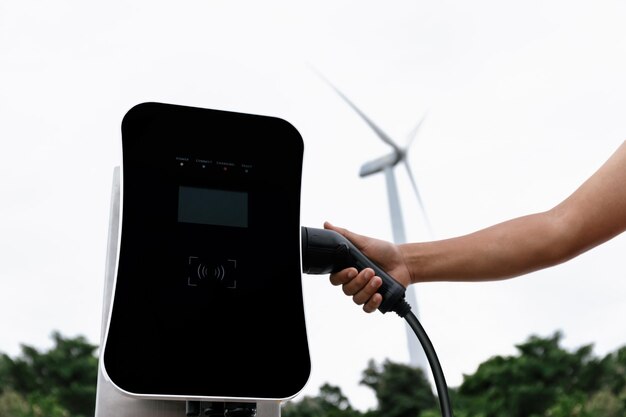 Steek de stekker met de hand in de EV met progressieve natuurlijke landschappen en windturbines