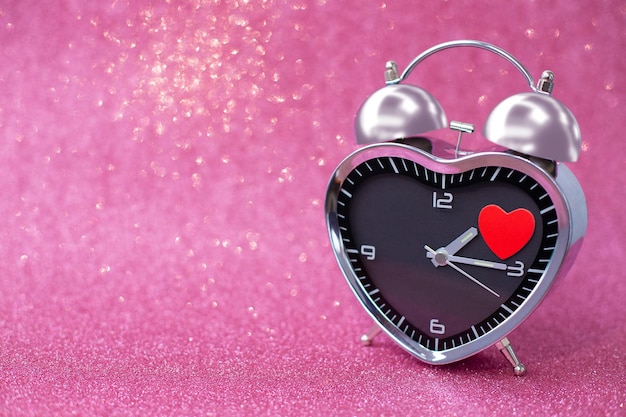 Foto sveglia in acciaio a forma di cuore con un cuore rosso su sfondo rosa glitterato lucido san valentino