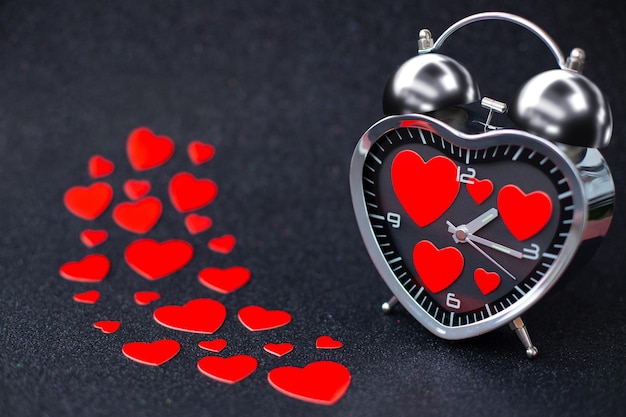 Foto sveglia in acciaio a forma di cuore con cuori rossi all'interno su sfondo nero glitterato lucido buon san valentino