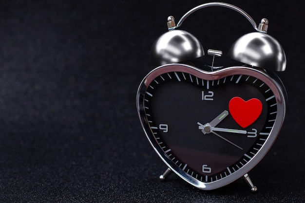 写真 黒い光沢のある背景に赤いハートのハートの形をしたスチール時計アラームハッピーバレンタインデー