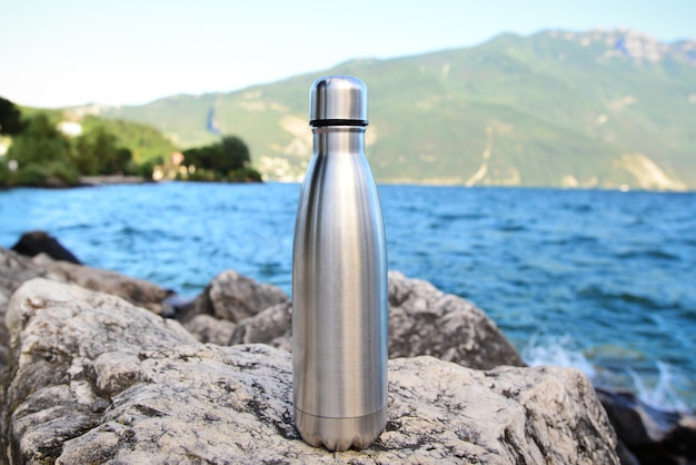 Steel eco thermo water bottle on the wall of the lake in the mountains be plastic free