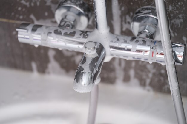 Steel faucet with soap foam in bathroom closeup