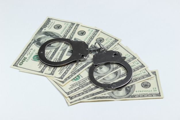 Steel handcuffs and one hundred dollar bills on a white background.