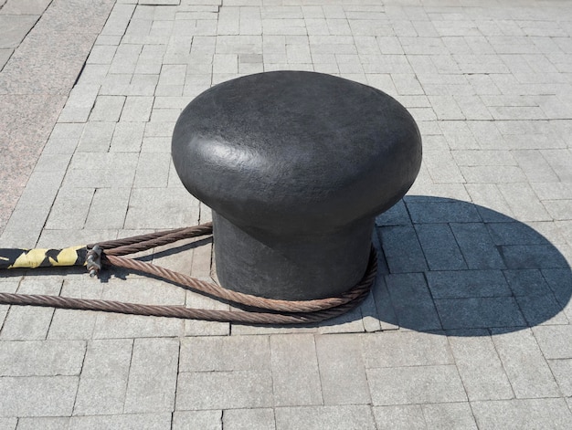 Steel mooring bollard with knotted ropes anchoring ships in sea or river port