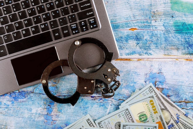 Steel police handcuffs on a pile of one hundred dollar bills with computer keyboard, technology cyber crime internet