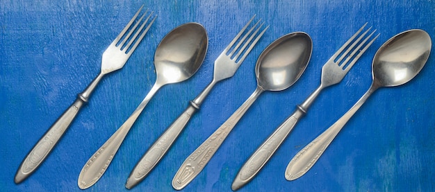 Steel spoons and forks on a blue wooden surface. Top view.