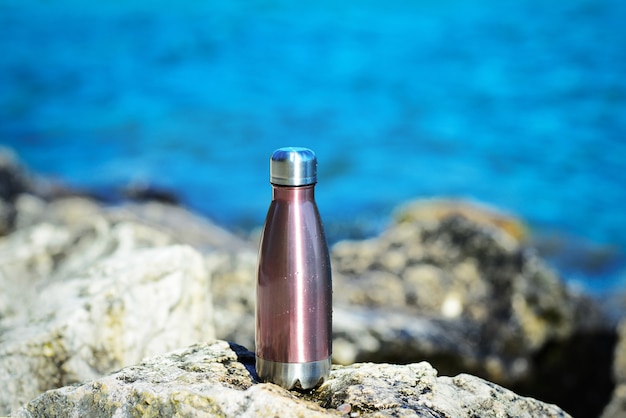 Стальная термо-бутылка для воды на фоне чистой воды озера бирюзового оттенка Copy space concept