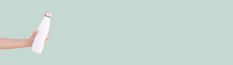 Steel thermo water bottle in female hand on pastel green surface. Panoramic photo with copy space.