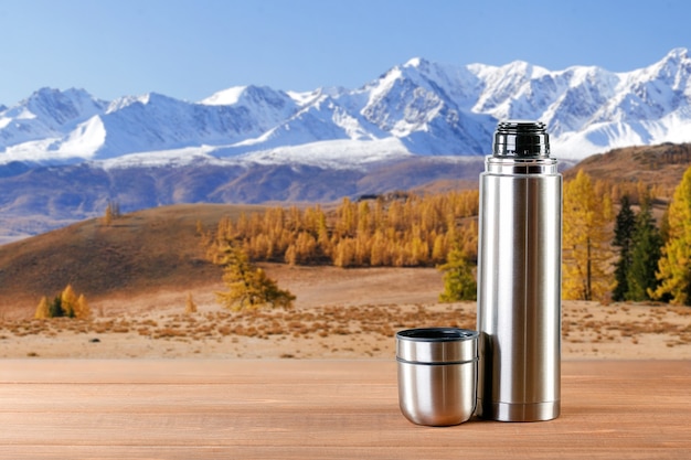 Steel Thermos on wooden table in mountains background.