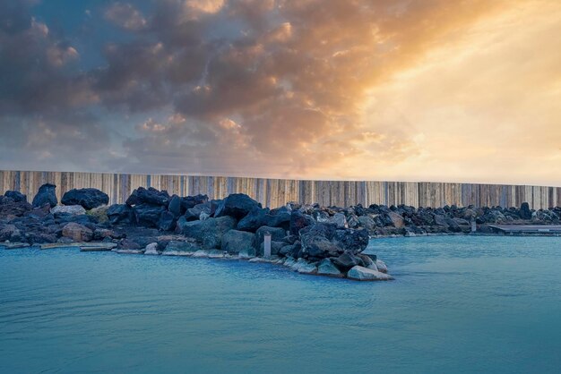 Steenen bij geothermische spa in blauwe lagune tegen bewolkte lucht tijdens zonsondergang