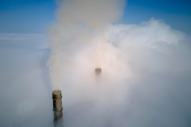 Steenkoolcentrale hoge leidingen met zwarte rook die omhoog bewegen over wolken die de atmosfeer vervuilen Productie van elektrische energie met fossielbrandstofconcept