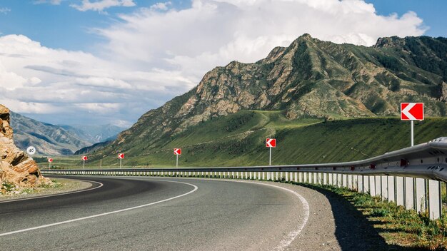 A steep curve of the road against the backdrop of beautiful mountains and cloudy sky