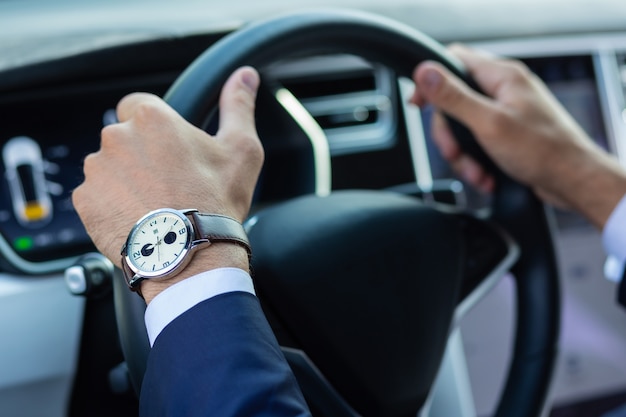 Steering wheel. Close up of businessman wearing hand watch holding steering wheel