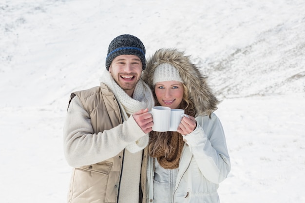 Stel in warme kleding met koffiekoppen op gesneeuwd landschap