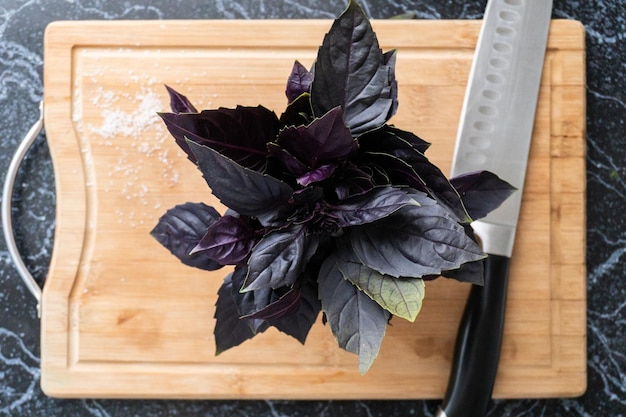 Stelletje basilicum blaadjes en mes op het houten bord in de keuken. Veganistisch eten vanuit bovenaanzicht.