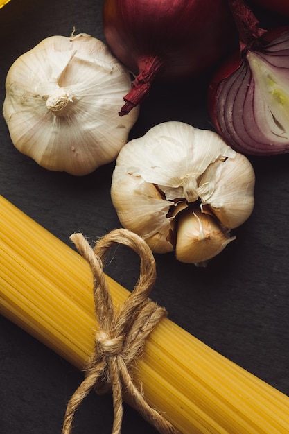 Stelletje spaghetti met een touw boog. Twee knoflookbollen en twee uien die dichtbij liggen