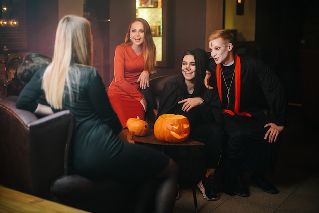 Stelletje vier vrienden die plezier hebben met het vieren van Halloween in café. Guy is verkleed als vreselijke priester en monster. Mooi sexy meisje in rode jurk. Gesneden pompoen op tafel