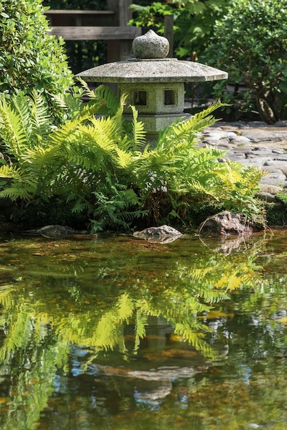 stenen lantaarn wordt weerspiegeld in het water van een vijver in een Japanse tuin