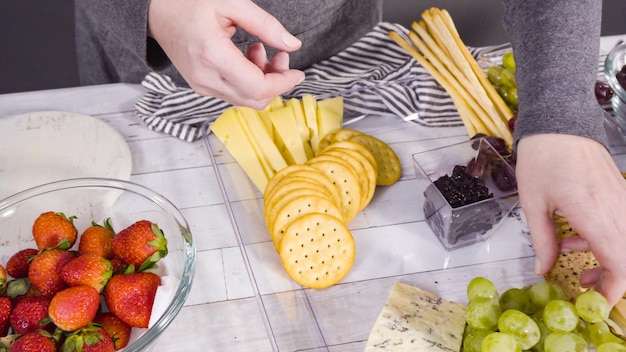 Step by step. Arranging cheese platter with fresh fruits, gourmet cheese, and crackers.