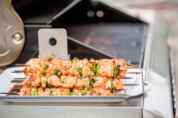 ステップバイステップ。屋外ガスグリルの隣にあるホワイトメタルのサービングトレイに鶏肉の焼き鳥。