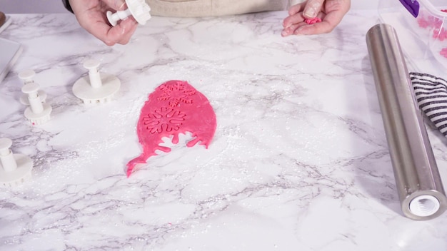 Step by step. Cutting out snowflakes with cookie cutters out of pink fondant on a marble counter.