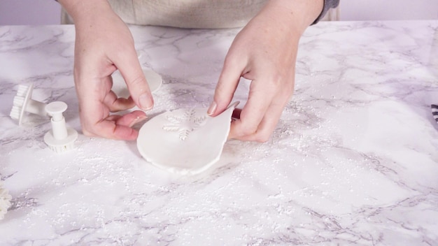 Step by step. Cutting out snowflakes with cookie cutters out of white fondant on a marble counter.