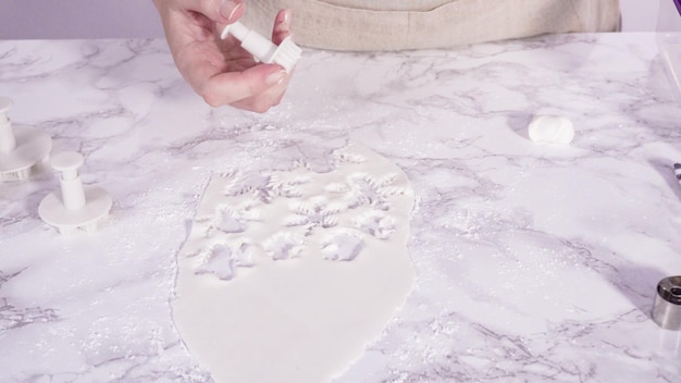 Step by step. Cutting out snowflakes with cookie cutters out of white fondant on a marble counter.