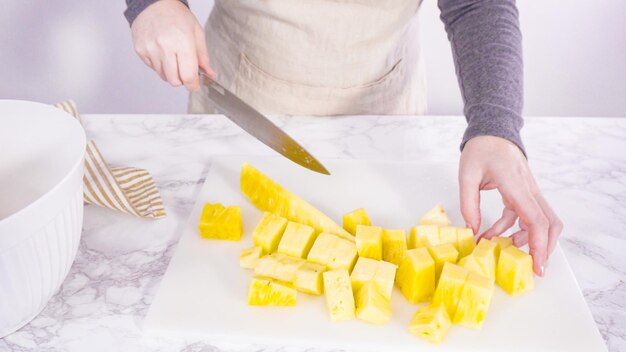 Step by step. Cutting pineapple on a white cutting board.