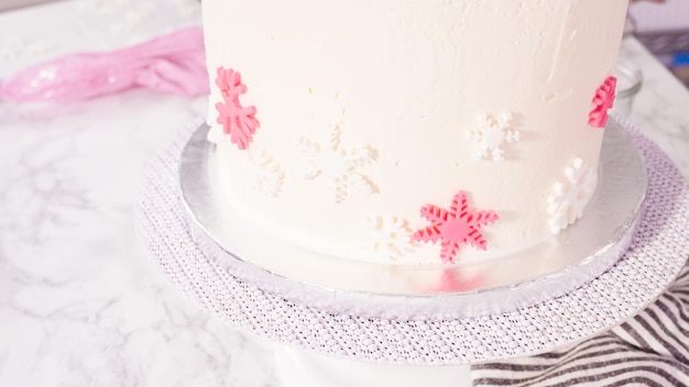 단계별로. 분홍색과 흰색 퐁당 눈송이로 둥근 펀페티 케이크를 장식합니다.