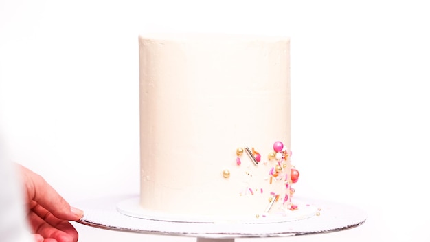 Step by step. Decorating tall birthday cake with a pink sprinkles.