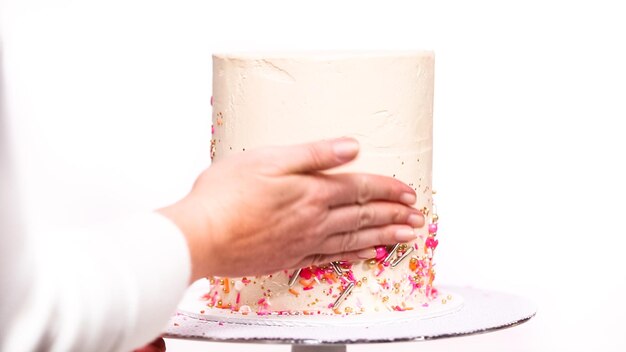 Step by step. Decorating tall birthday cake with a pink sprinkles.