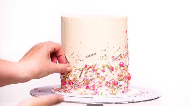 Step by step. Decorating tall birthday cake with a pink sprinkles.
