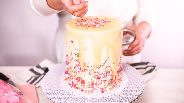 Step by step. Decorating tall birthday cake with a pink sprinkles.