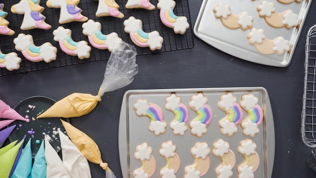 Step by step. Flat lay. Decorating unicorn sugar cookies with royal icing on baking sheet.