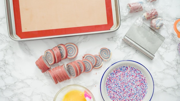 단계별로. 플랫 레이. 빨간색, 흰색 및 파란색 바람개비 설탕 쿠키의 가장자리를 스프링클에 롤링합니다.