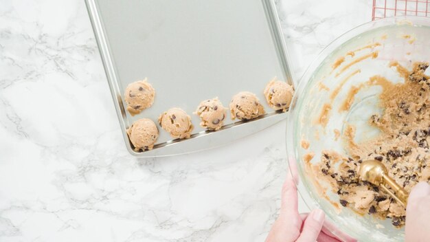 Step by step. Flat lay. Scooping homemade chocolate chip cookies with metal dough scoop to the baking sheet.