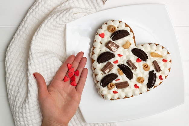 Photo step-by-step heart-shaped cake recipe instructions. step 12: decorate the cake with chocolate chips, waffles, cookies. flat lay.