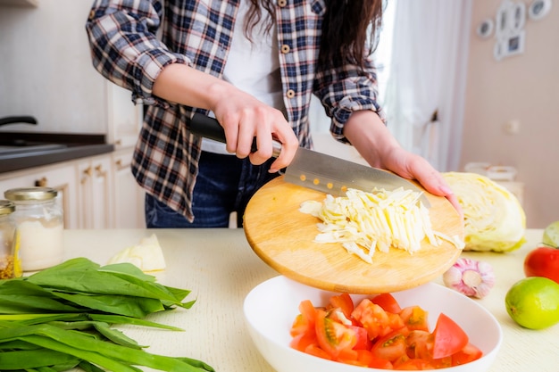 キャベツ、トマト、ネギ、スパイス、オリーブオイルを使った野菜サラダの作り方の手順。ステップ2.キャベツを細かく刻み、プレートにトマトを加えます。
