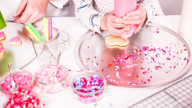 Photo step by step. little girl decarting sugar cookies with royal icing and sprinkles for valentine's day.