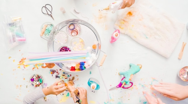 Step by step. Little girls decorating paper mache unicorn with glitter and paper flowers.