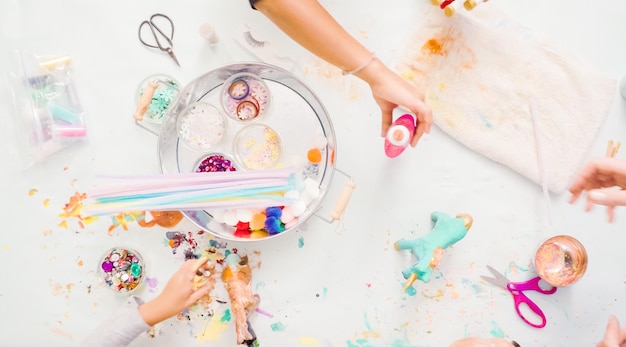 Step by step. Little girls decorating paper mache unicorn with glitter and paper flowers.